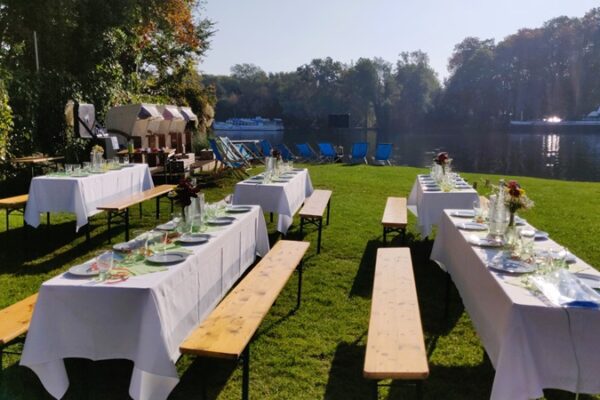 Sommerwiese mit festlich geschmückten Bierbanken auf der grünen Wiese an der Spree.