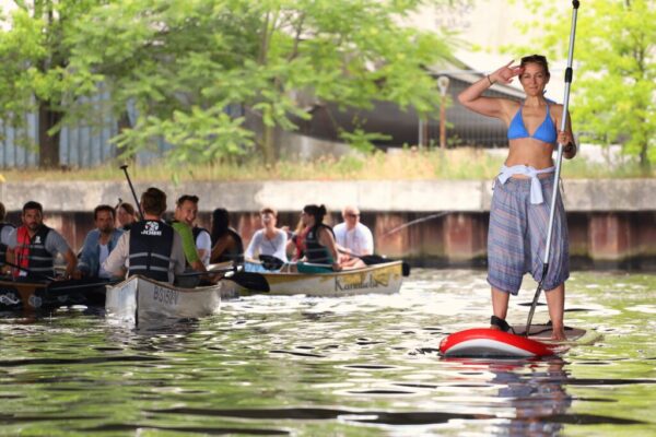 Eine Gruppe von Kanus auf der Spree mit einer Frau auf einem SUP-Board im Vordergund.