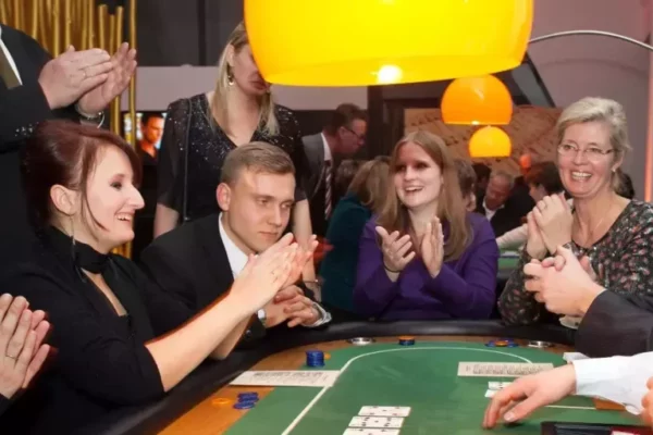 Mehrere Personen sitzen bei einer Firmenveranstaltung in Form von einem Casinoabend um einen Pokertisch herum und applaudieren dem Gewinner.